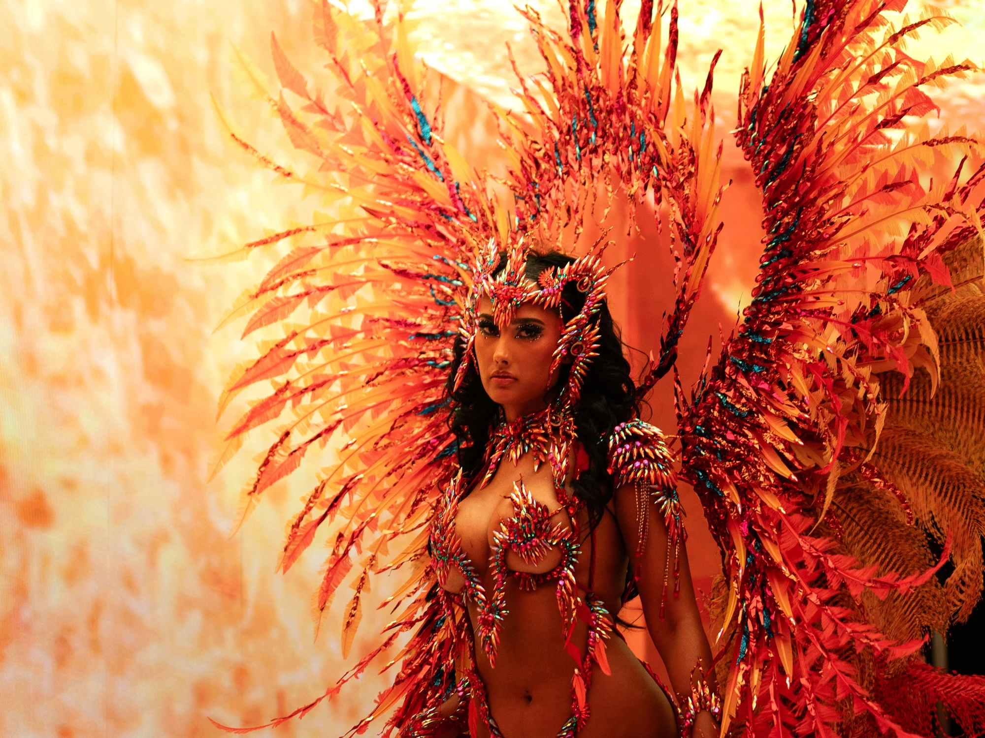 The EMBER costume shown in full — jewelled bra, belt and leg chains beneath a feathered backpack at full span.